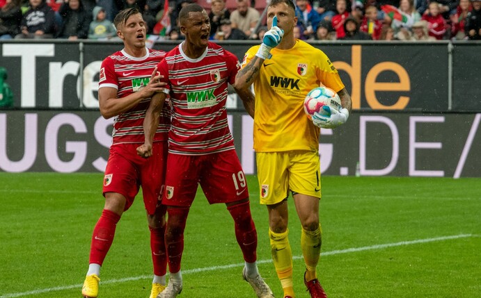 Augsburgs Torwart Rafal Gikiewicz (r) lässt sich nach dem gehaltenen Elfmeter von Emirdan Demirovic (l) und Felix Uduokhai feiern.