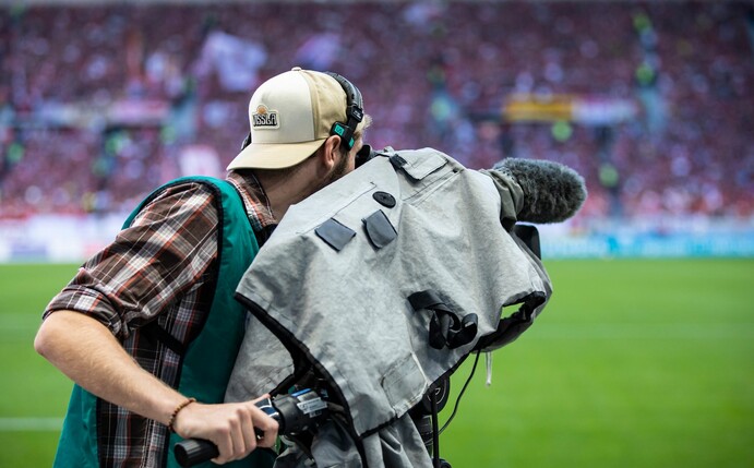 Ein Kameramann steht am Spielfeldrand und filmt ein Fußballspiel.