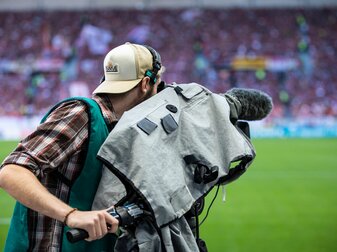 Ein Kameramann steht am Spielfeldrand und filmt ein Fußballspiel. Ein Kameramann steht am Spielfeldrand und filmt ein Fußballspiel.