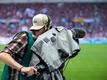 Ein Kameramann steht am Spielfeldrand und filmt ein Fußballspiel.