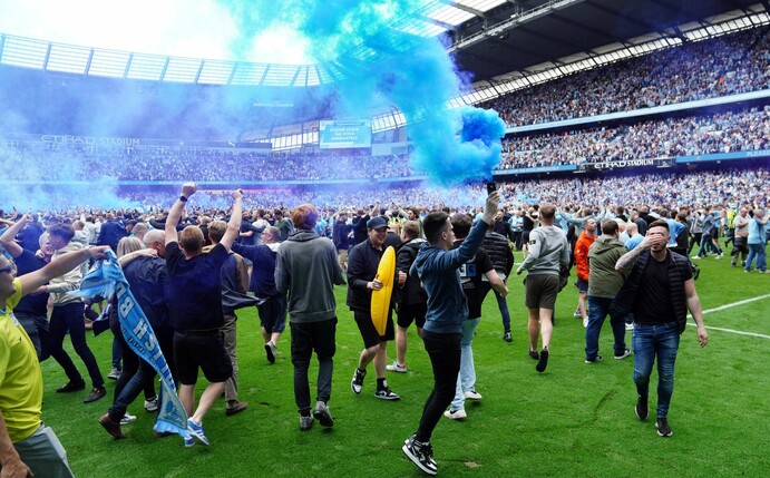 Fans von Manchester City stürmen das Spielfeld und jubeln über den Gewinn der englischen Meisterschaft.