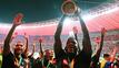 Leverkusens Victor Boniface (r) hält den Pokal jubelnd hoch, während seine Teamkollegen feiern.