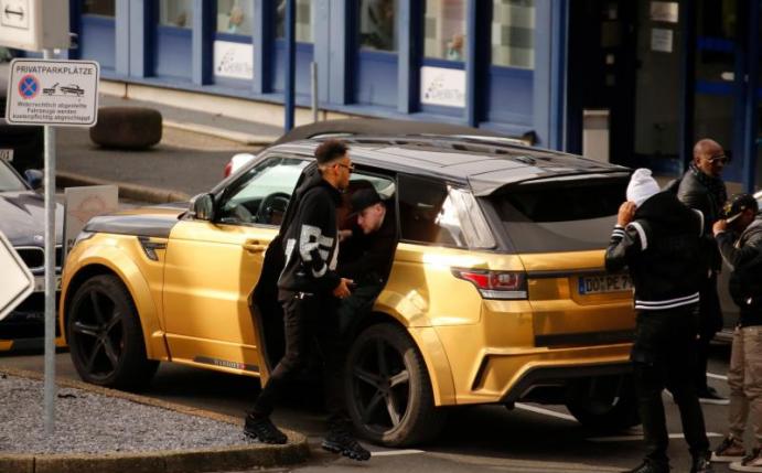 Pierre-Emerick Aubameyang (l) kommt mit einem goldfarbenen Land Rover zum Dortmunder Flughafen. Foto: Guido Kirchner