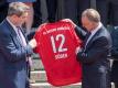 Karl-Heinz Rummenigge überreicht Markus Söder ein Trikot mit der Nummer 12 und der Aufschrift «Söder». Foto: Peter Kneffel