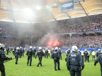 Feuerwerkskörper brennen vor dem Abpfiff auf der Tribüne, während Polizisten auf dem Spielfeld stehen. Foto: Daniel Bockwoldt Feuerwerkskörper brennen vor dem Abpfiff auf der Tribüne, während Polizisten auf dem Spielfeld stehen. Foto: Daniel Bockwoldt
