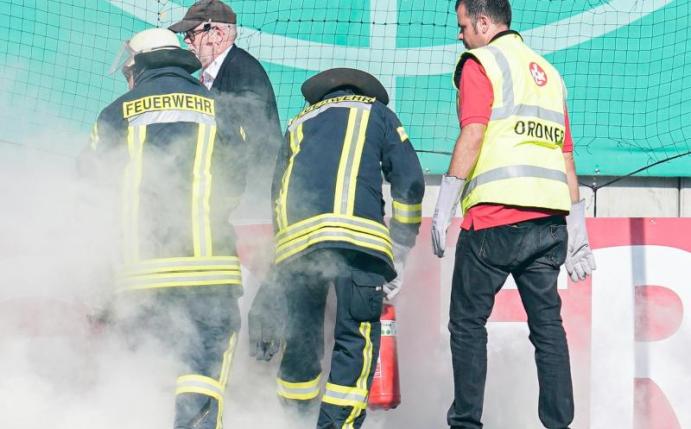 Feuerwehrleute löschen brennende Bengalos, die von Mainzer Fans aufs Spielfeld geworfen wurden. Foto: Uwe Anspach/dpa