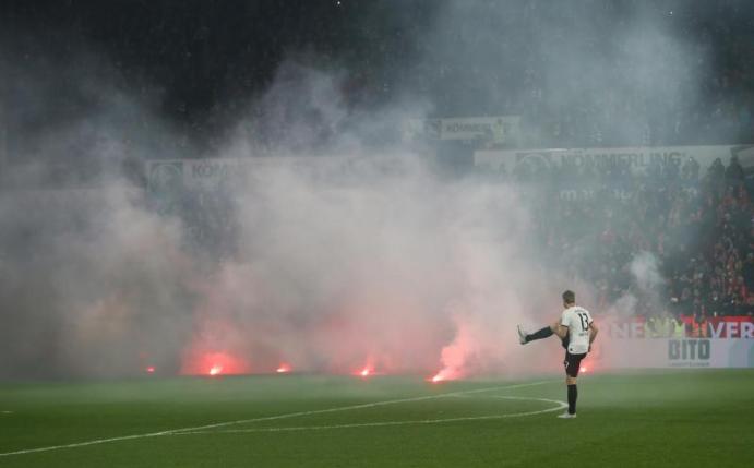 Dichte Rauchschwaden durchziehen das Mainzer Stadion, nachdem Feuerwerkskörper aus dem Gästeblock auf dem Rasen gelandet sind. Foto: Thomas Frey/dpa