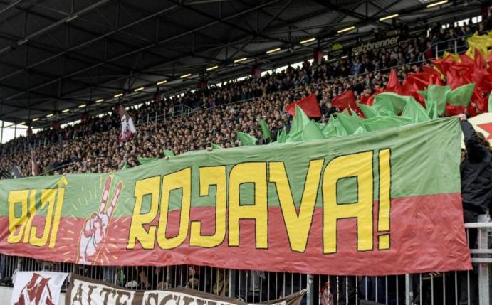 Fans von St. Pauli halten ein Banner mit dem Schriftzug «Biji Rojava» («Es lebe Rojava») in die Höhe. Foto: Axel Heimken/dpa