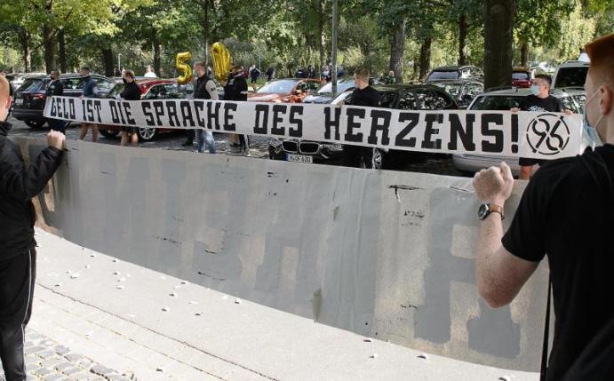 Fans von Hannover 96 stehen mit einem Banner «Geld ist die Sprache des Herzens» am VIP-Eingang des Stadions vor dem Spiel Spalier. Foto: Swen Pförtner/dpa