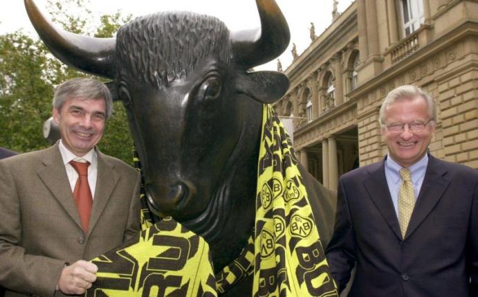 Gerd Niebaum (r), damaliger BVB-Präsident, und der damalige BVB-Manager Michael Meier stehen am 31.10.2000 vor der Frankfurter Börse mit einem übergroßen Fanschal am Bronzebullen. Foto: Arne Dedert/dpa/Archivbild