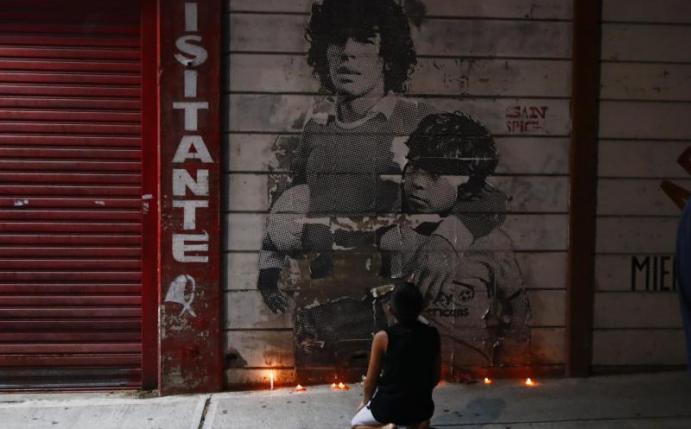 Ein Junge kniet vor einem mit Kerzen dekorierten Wandbild von Diego Maradona in Argentinien. Foto: Marcos Brindicci/AP/dpa