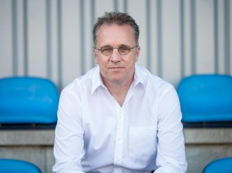 Tim Meyer, DFB-Chefmediziner, sitzt auf überdachten Sitzplätzen auf einem Fußballplatz. Foto: Oliver Dietze/dpa/Archivbild