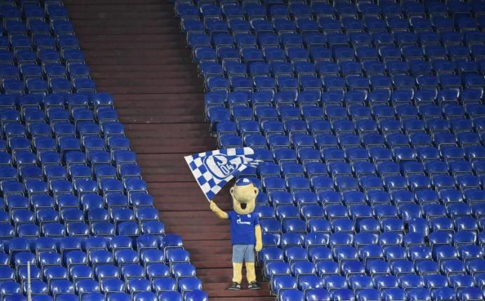 Schalke-Maskottchen Erwin schwenkt auf der sonst leeren Tribüne während des Revierderbys eine Fahne. Foto: Martin Meissner/Pool AP/dpa