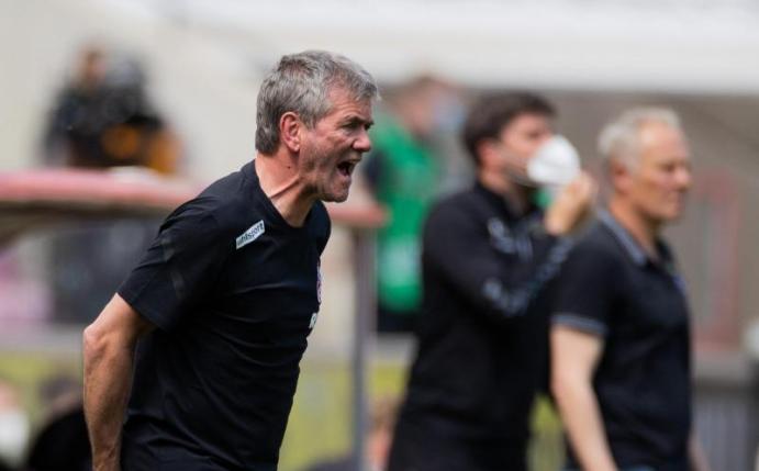 Kölns Trainer Friedhelm Funkel versucht seine Spieler auf dem Platz zu erreichen - im Hintergrund steht Freiburgs Trainer Christian Streich. Foto: Rolf Vennenbernd/dpa