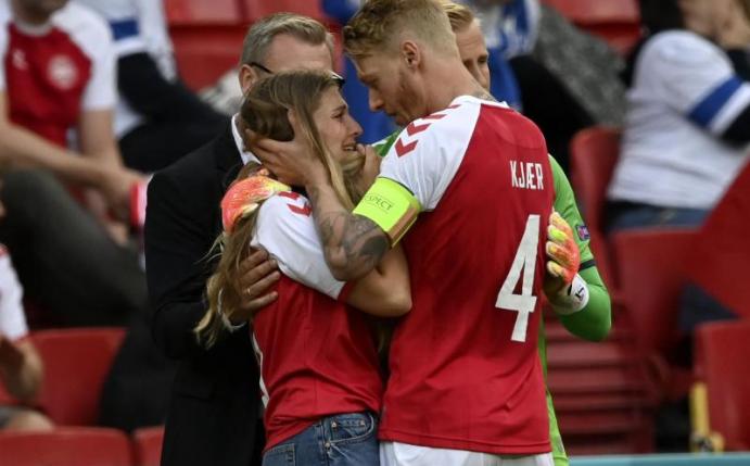 Dänemarks Mannschaftskapitän Simon Kjaer (r) spricht mit einer Frau, die das Trikot des dänischen Spielers Eriksen trägt, der auf einer Trage vom Feld gebracht wurde. Foto: Stuart Franklin/Getty Pool/AP/dpa
