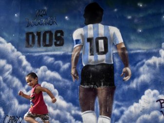 «Hier ruht Gott», steht an einem Wandgemälde zu Ehren des verstorbenen Fußballstars Maradona vom Künstler Onehumano, an dem ein Kind vorbei rennt. Foto: Fernando Gens/dpa