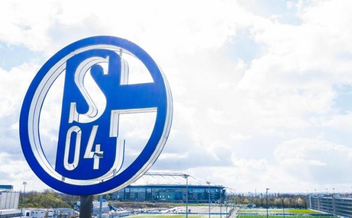 Im Vordergrund dreht sich das Logo des FC Schalke 04. Foto: Guido Kirchner/dpa/Archivbild