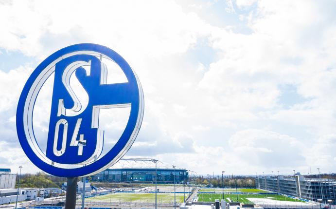 Im Vordergrund dreht sich das Logo des FC Schalke auf der Geschäftsstelle, im Hintergrund steht die Veltins-Arena.