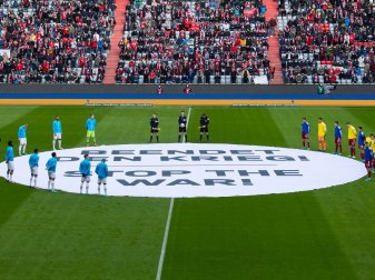 Die Spieler von München und von Leverkusen stehen um ein Banner mit «Beendet den Krieg! - Stop the War!». Die Spieler von München und von Leverkusen stehen um ein Banner mit «Beendet den Krieg! - Stop the War!».