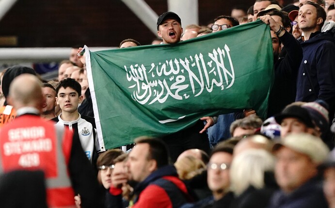 Ein Fan von Newcastle United hält die Fahne von Saudi-Arabien während eines Spiels hoch.