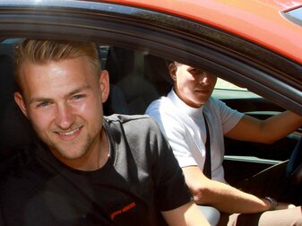 Matthijs de Ligt (l) lächelt beim Verlassen der Bayern-Geschäftsstelle aus dem Fenster eines Autos.
