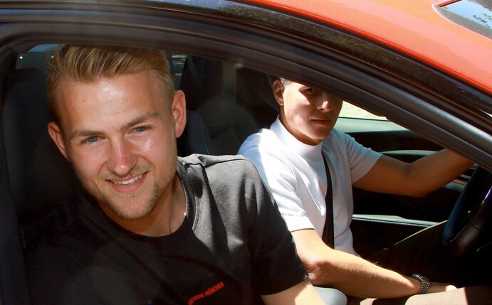 Matthijs de Ligt (l) lächelt beim Verlassen der Bayern-Geschäftsstelle aus dem Fenster eines Autos.