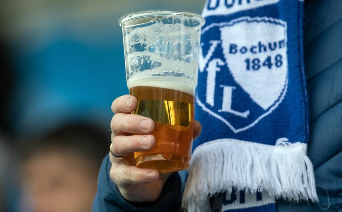 Ein Fan des VfL Bochum hält einen Becher mit Bier in der Hand.